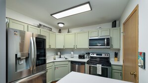 Uma cozinha moderna com eletrodomésticos de aço inoxidável, armários verde-claros e bancada branca.