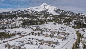 Estância coberta de neve com vários edifícios, área de estacionamento e uma montanha ao fundo.