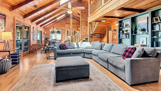 A spacious living area with a large gray sectional sofa, a matching ottoman, and a wooden ceiling with exposed beams. - Ellijay Walnut Mountain Cabin - Hot Tub, Fire Table, Pet Friendly and Views (Ellijay)