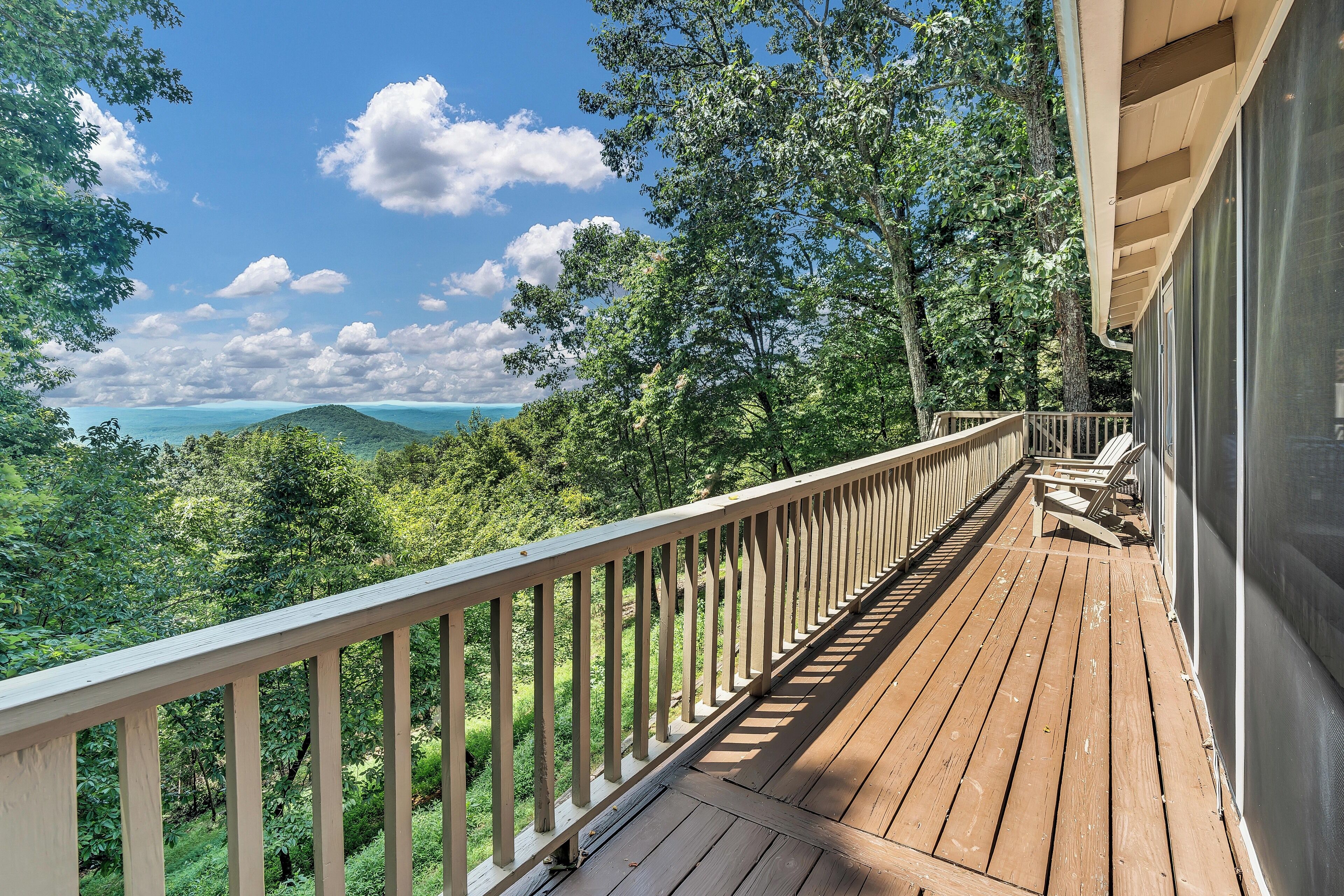 Une terrasse en bois dotée d’une balustrade, qui offre une vue sur un paysage luxuriant et une étendue d’eau.