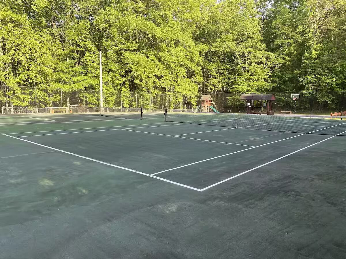 Ein Tennisplatz im Freien mit Netz, umgeben von Bäumen und einem kleinen Pavillon.