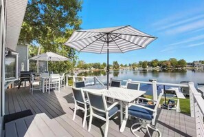 Eine Terrasse mit Gartenmöbeln, einem großen Sonnenschirm und Blick auf einen See.