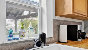 Una cocina con ventana, un lavamanos, una cafetera y un refrigerador.