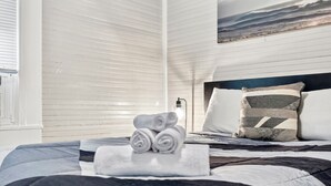 Una cama bien hecha con toallas enrolladas, un cabecero con almohadas y una ventana con persianas.