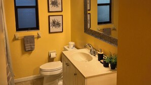 Een badkamer met een gele wand, een wit toilet, een wastafel met spiegel en ingelijste foto's aan de muur.