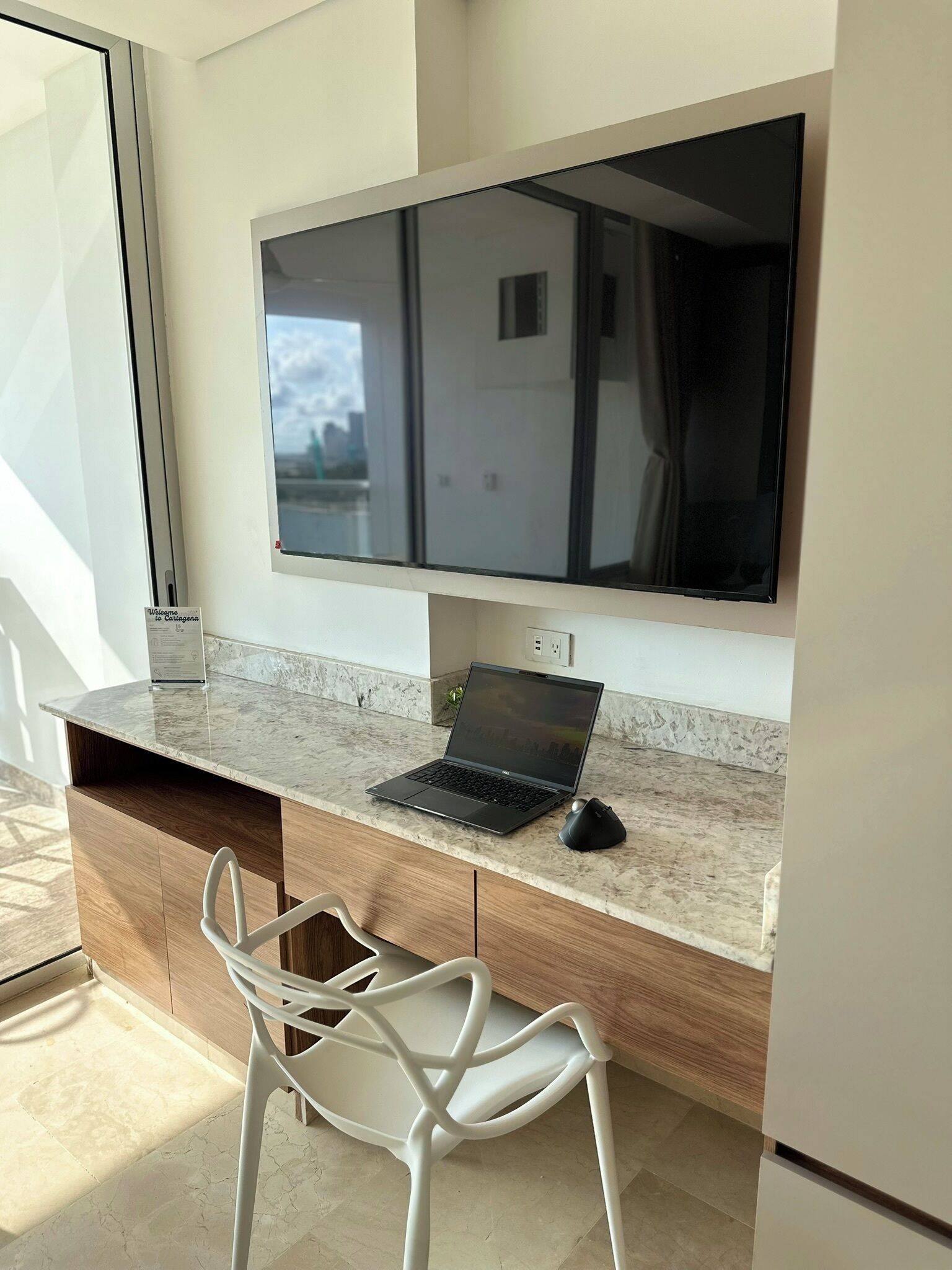 Een moderne keuken met een marmeren aanrecht, een laptop, een flatscreen televisie en een witte stoel.