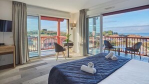 A hotel room with a bed, a desk, a chair, a table, and a balcony with a view. - Hotel Erromardie Plage by Odalys (Saint-Jean-de-Luz)
