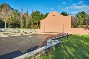 Un espace de stationnement délimité par une barrière en béton, un escalier menant à l’entrée d’un bâtiment et un ciel dégagé.