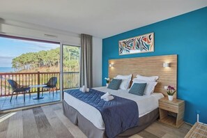 Quarto com uma cama grande, cabeceira de madeira, mesa de cabeceira e vista para o oceano através de uma porta de correr.