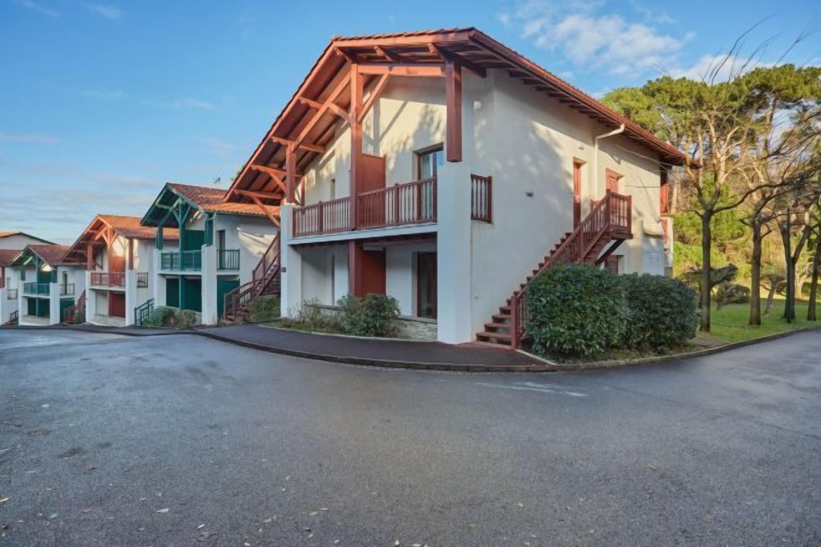 A row of two-story buildings with balconies, a paved driveway, and a clear sky.
