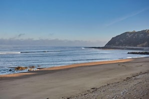Une plage avec un ciel dégagé, une mer calme et une falaise rocheuse en arrière-plan.