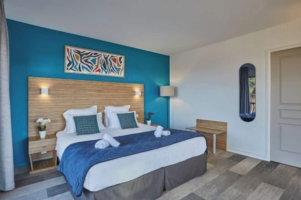 Ein modernes Hotelzimmer mit einem großen Bett, einem hölzernen Kopfteil, einer blauen Akzentwand und einem Gemälde.
