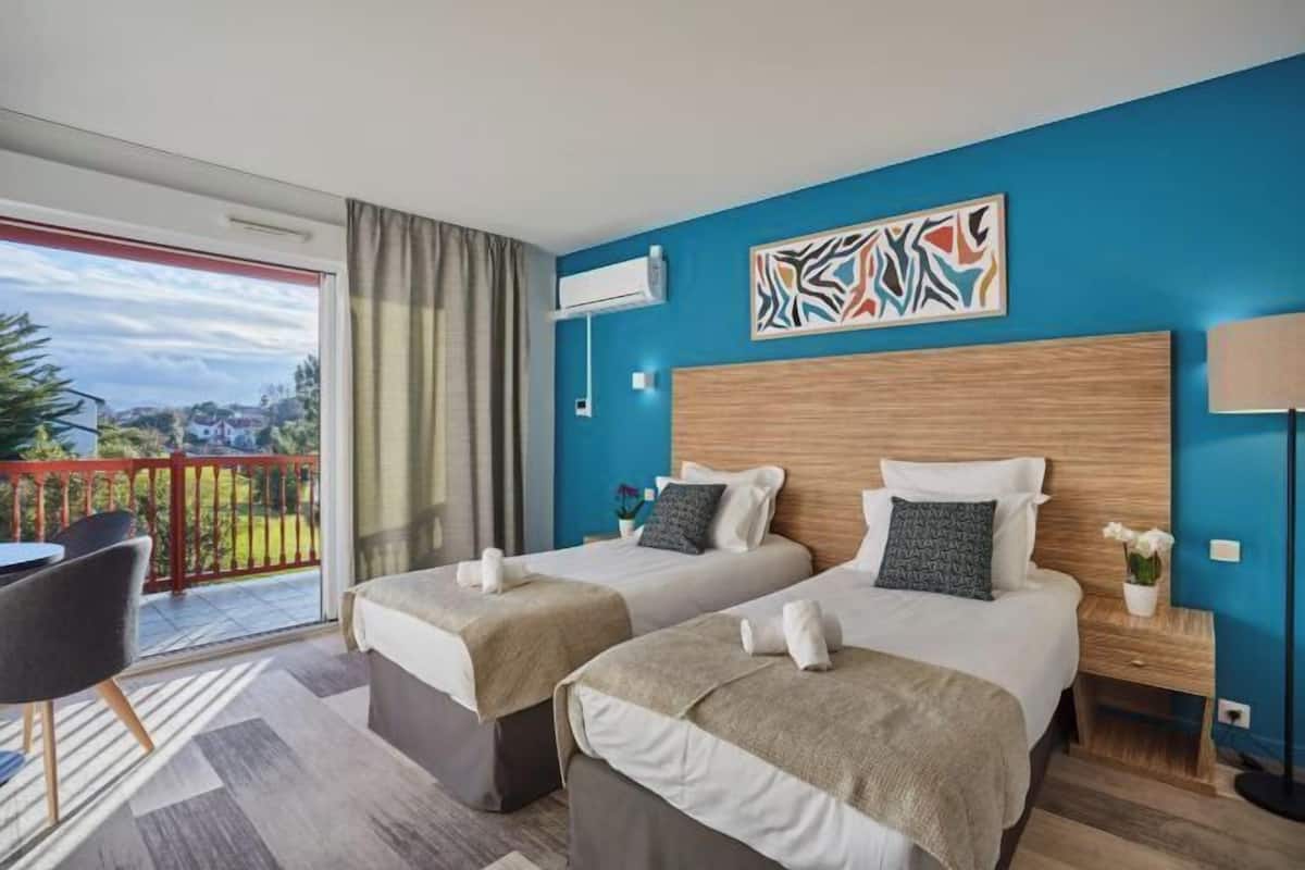 Ein Hotelzimmer mit zwei Betten, einem Balkon mit roter Geländer und einer blauen Akzentwand.