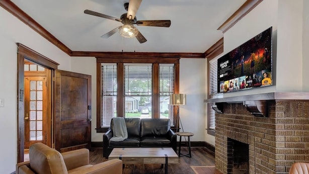 A living room with a fireplace, a television mounted on the wall, and a ceiling fan.