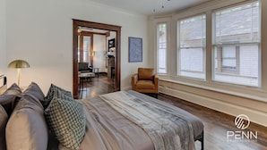 A spacious bedroom with a large bed, a ceiling fan, and a view of the outside through large windows.