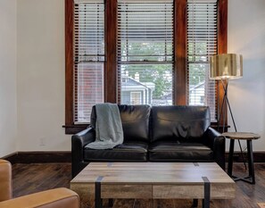 A living room with a black leather sofa, a wooden coffee table, and a floor lamp. - Spacious 3-in-1 Vintage Brick Escape (Memphis)