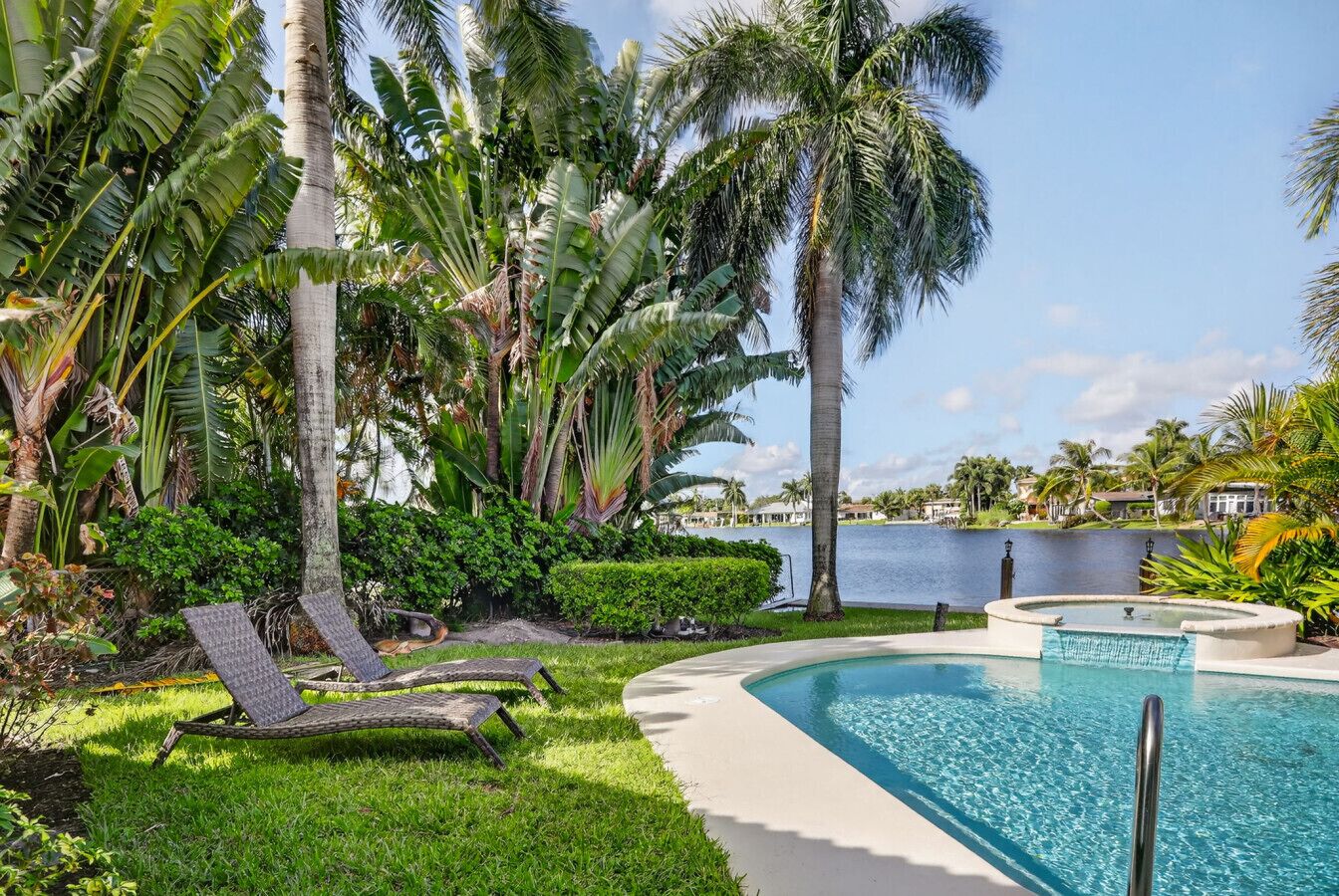 A pool area with lounge chairs, palm trees, and a view of a body of water.