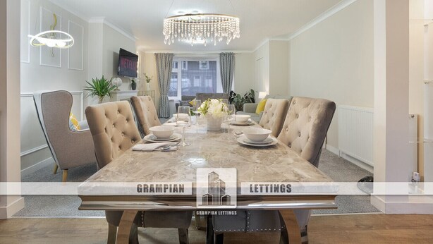 A dining room with a marble table, upholstered chairs, and a chandelier.