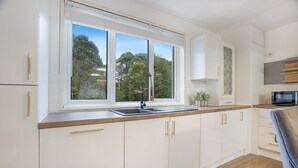 A modern kitchen with white cabinets, a double sink, and a large window providing a view of trees.