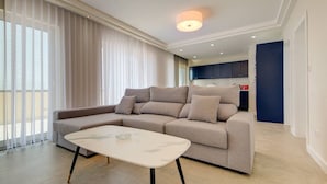 A modern living room with a beige sectional sofa, a white coffee table, and large windows with sheer curtains. - Stylish Gozo Penthouse Spacious and Quiet Terrace (Nadur)