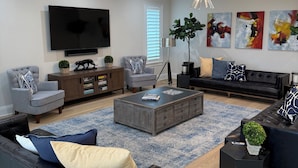 Ein modernes Wohnzimmer mit Flachbildfernseher, grauem Sofa, schwarzem Ledersofa, Couchtisch und abstrakten Wandbildern.