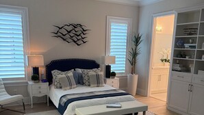 Ein Schlafzimmer mit einem großen Bett, Nachttischen, einer Bank, einer Wanddekoration und einem Regal mit verschiedenen Gegenständen.