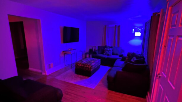A living room with a sofa, ottoman, and a flat-screen TV mounted on the wall. - 3-bedroom Beach House in Beautiful Charlotte near Beach with AC/Heat and Wi-Fi (Rochester)