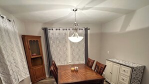 A dining room with a wooden table, chairs, a chandelier, a patterned rug, a cabinet, and a window with curtains. - 3-bedroom Beach House in Beautiful Charlotte near Beach with AC/Heat and Wi-Fi (Rochester)