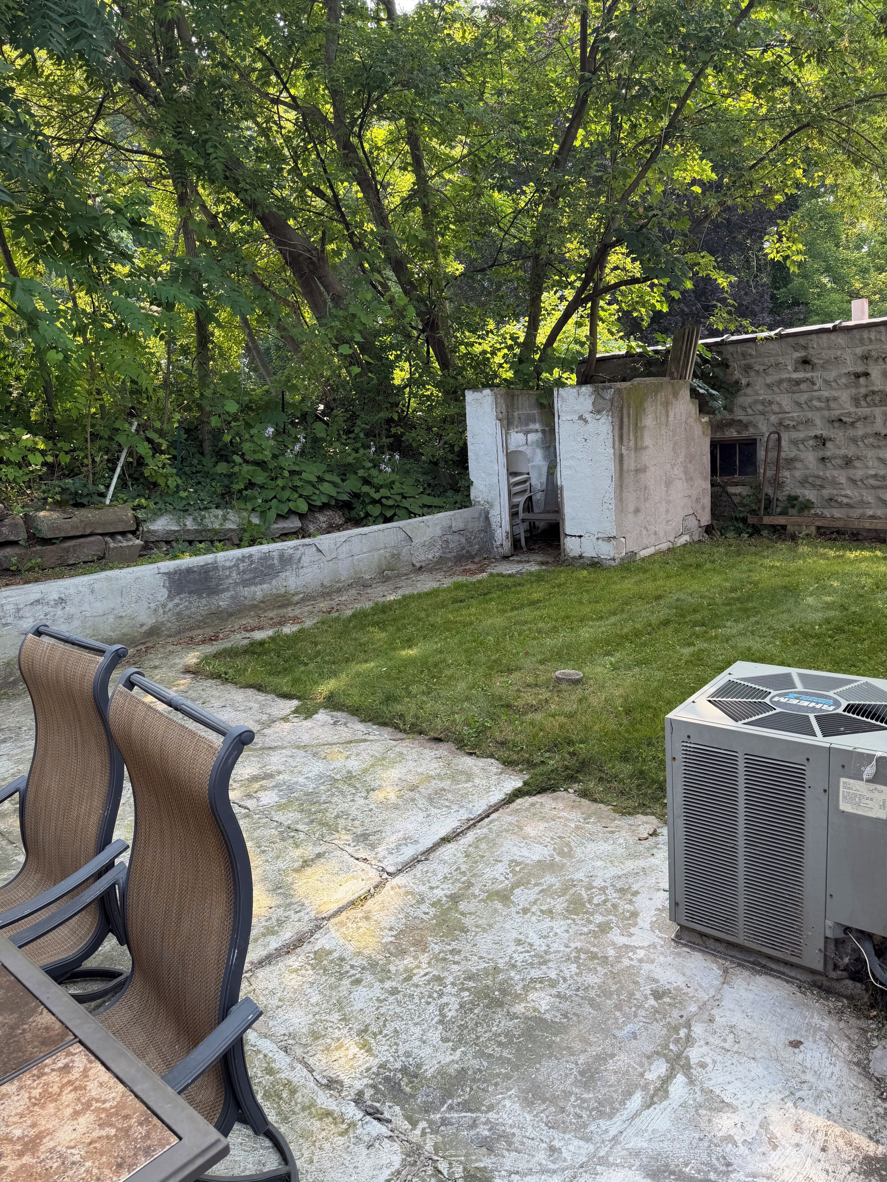Un espace extérieur aménagé en terrasse, doté d’un sol en béton, de sièges et d’un appareil de climatisation.