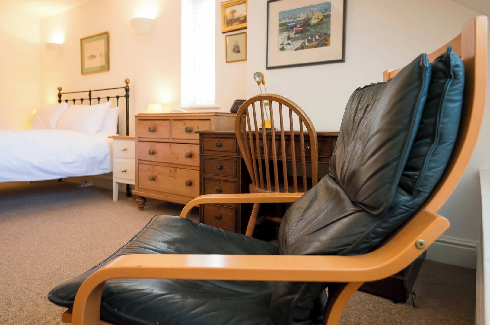 Une chambre à coucher comprenant un lit, une commode en bois, une chaise avec un siège en cuir et un bureau avec une lampe.