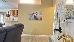Ein Wohnzimmer mit einem grauen Sofa, einem Gemälde eines Pferdes und einem dekorativen Elefanten auf einer strukturierten weißen Fläche.