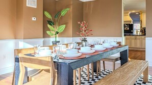 A dining area with a long table set for six, surrounded by wooden chairs. A potted plant and a vase with flowers are on the table. - 
Spacious 5-Bedroom Retreat Minutes from Washington (Virginia)