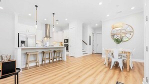 Une cuisine moderne avec des meubles blancs, un îlot central, des tabourets de bar et des luminaires suspendus.