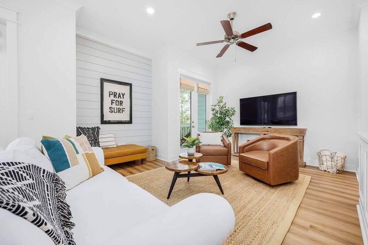 A living room with a sofa, two armchairs, a coffee table, a TV, and a ceiling fan.