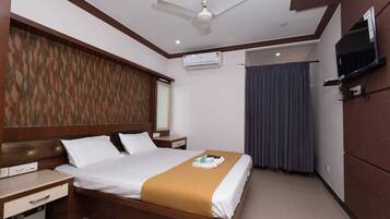 A hotel room with a bed, bedside tables, a TV, an air conditioning unit, and a ceiling fan.