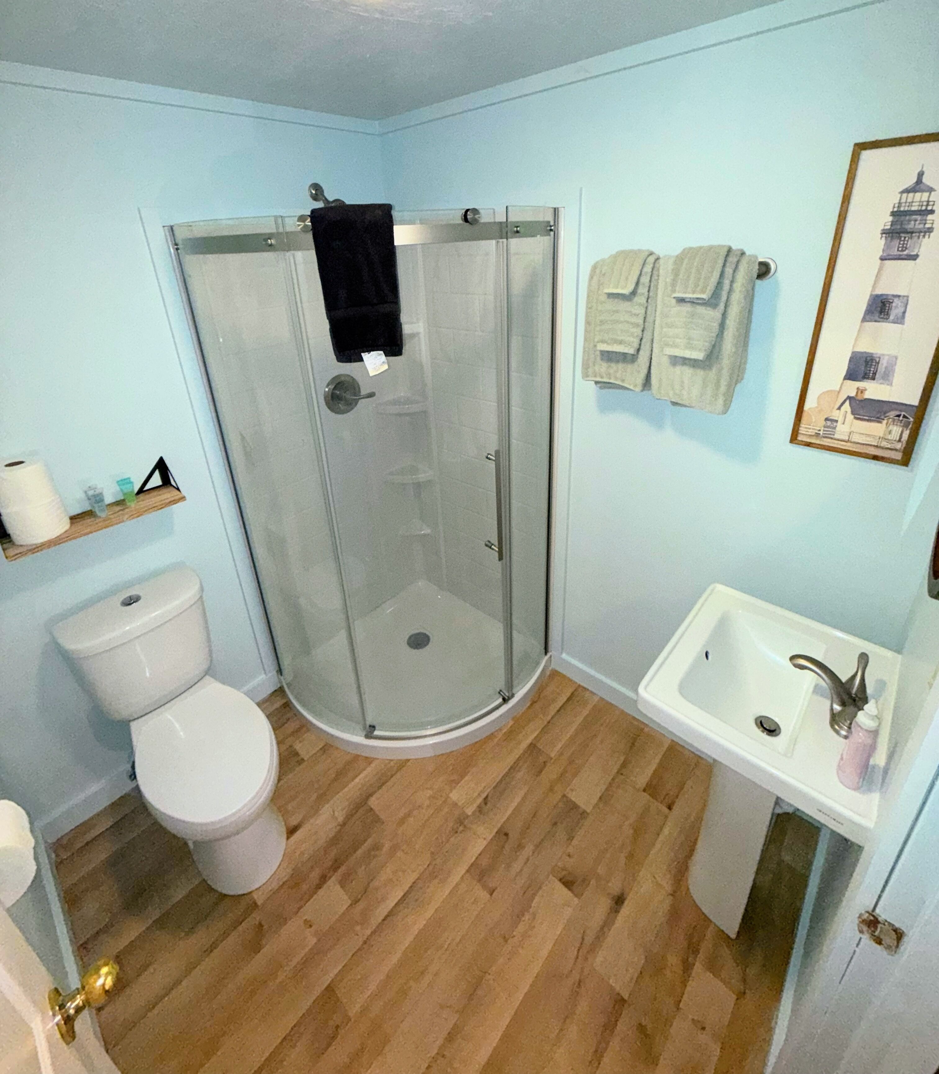 Casa de banho com cabine de duche em vidro, sanita e lavatório com espelho.