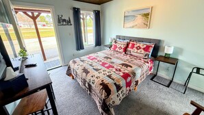 A bedroom with a large bed, a desk, a chair, a nightstand, and a window with curtains. - Peninsula Point Lodge (Rapid River)
