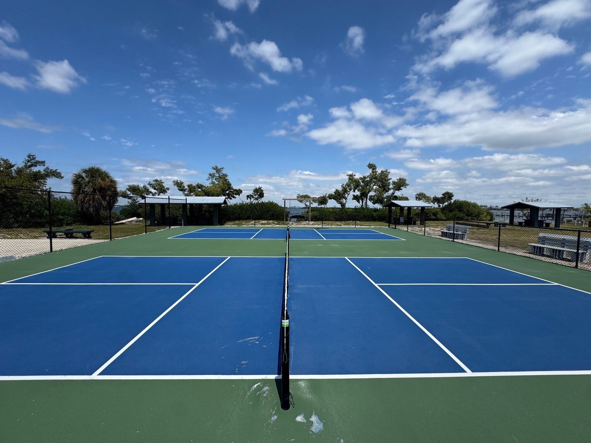 Un court de tennis avec un filet, entouré de bancs et d’arbres.