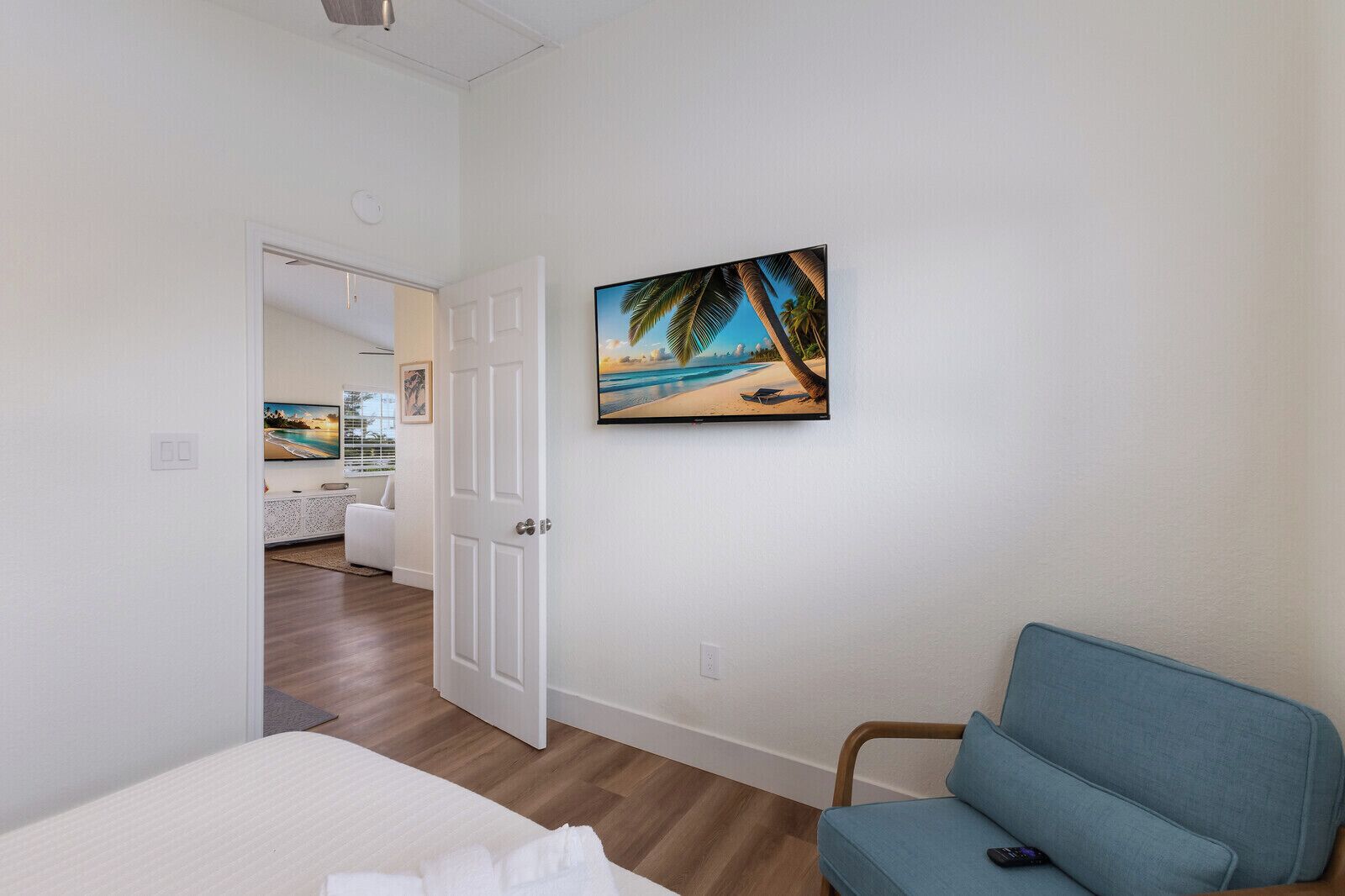 Une chambre à coucher avec un lit, une chaise bleue et un tableau représentant une scène de plage.