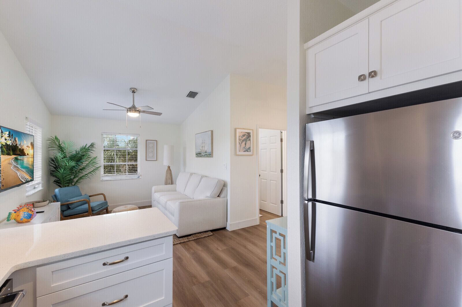 Una cocina moderna con armarios blancos, un refrigerador de acero inoxidable, un ventilador de techo y un comedor con mesa y sillas.