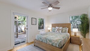 Quarto com cama de madeira, ventilador de teto e vista para o exterior através de uma porta de correr de vidro.