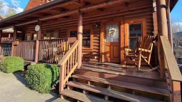 A wooden log cabin with a porch, a wooden staircase, and a wooden chair.