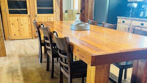 A wooden dining table with chairs, a kitchen area with cabinets and appliances, and a wooden floor. - Lake front Farm Cabin, Hot Tub, Star Gazing with Telescope, Fire pit (Kite)