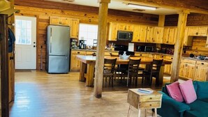 A spacious kitchen with wooden cabinets and a central island, a dining area with a wooden table and chairs, and a cozy seating area with a green sofa and a small rug. - Lake front Farm Cabin, Hot Tub, Star Gazing with Telescope, Fire pit (Kite)