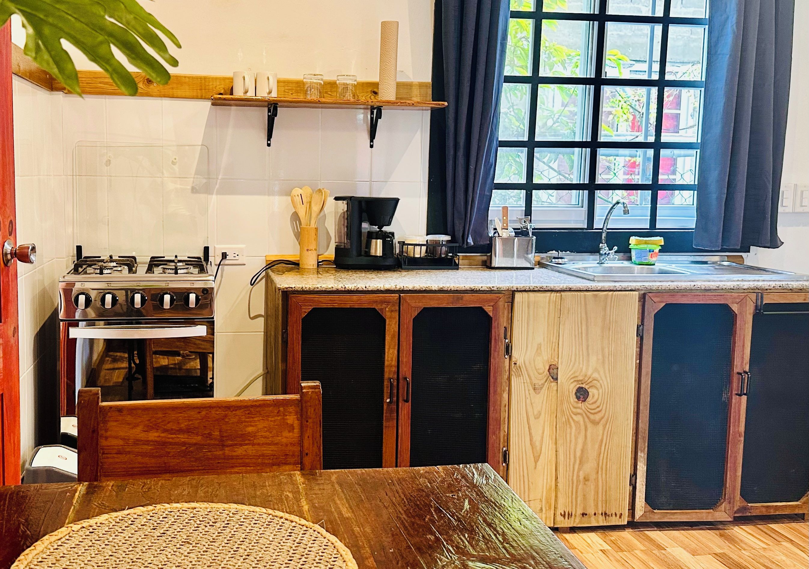 A kitchen with a gas stove, oven, wooden cabinets, a coffee maker, and a window with curtains.