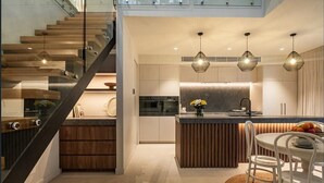 Een moderne keuken met een centraal eiland, een eethoek met witte stoelen en een trap met houten treden.
