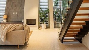 Een ruime woonkamer met een hoge plafond, een trap en grote ramen met uitzicht op bomen.
