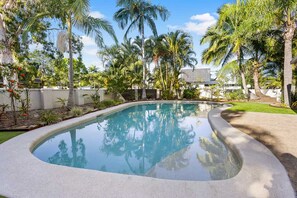 Ein Pool mit gewölbter Kante, umgeben von Palmen und einer weißen Mauer.