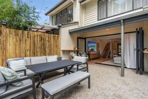 A covered patio with outdoor furniture, a wooden fence, and a view into the house. - The Noosa Villa Luxe Townhouse in Great Location (Noosa)