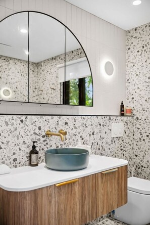 Ein Badezimmer mit freistehender Waschbecken, einem Spiegel und einer Toilette.